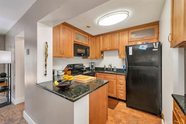 kitchen with brown cabinetry, black appliances, dark stone counters, and a sink