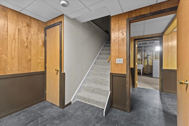 staircase with wood walls and a paneled ceiling