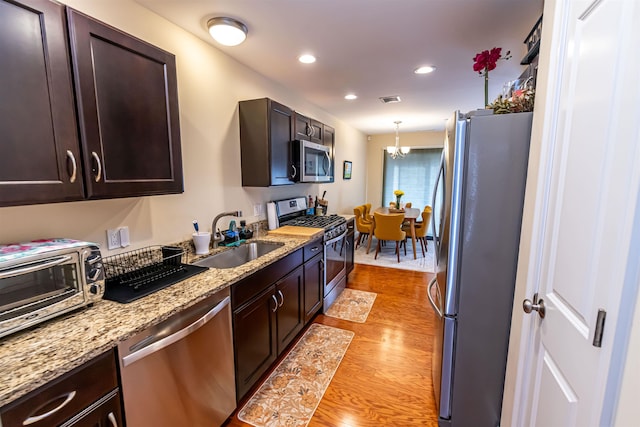 kitchen featuring visible vents, a sink, stainless steel appliances, light wood-style floors, and dark brown cabinets