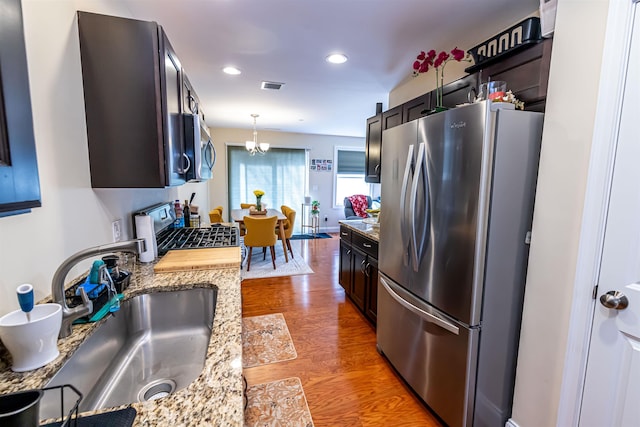 kitchen featuring visible vents, a sink, light stone counters, wood finished floors, and appliances with stainless steel finishes