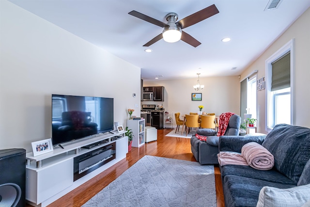 living area with ceiling fan with notable chandelier, recessed lighting, wood finished floors, and visible vents