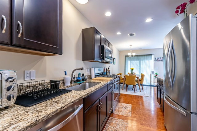 kitchen featuring light wood-type flooring, a notable chandelier, a sink, stainless steel appliances, and dark brown cabinetry