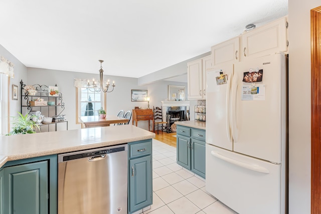 kitchen with blue cabinetry, light countertops, freestanding refrigerator, light tile patterned flooring, and stainless steel dishwasher