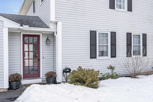 snow covered property entrance featuring a shingled roof