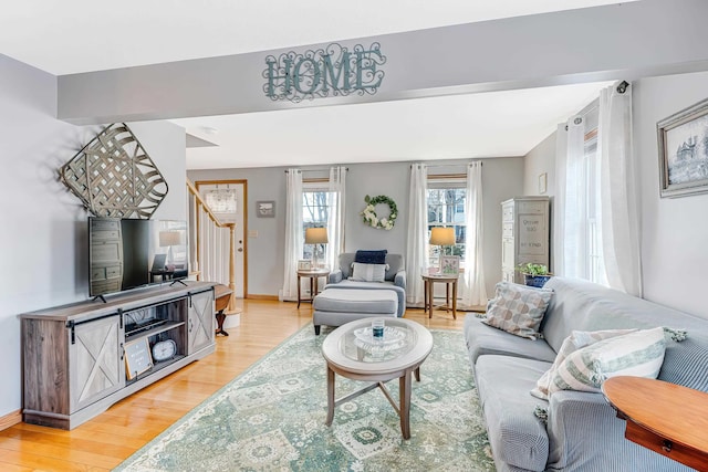 living area featuring baseboards, light wood-style floors, and stairs