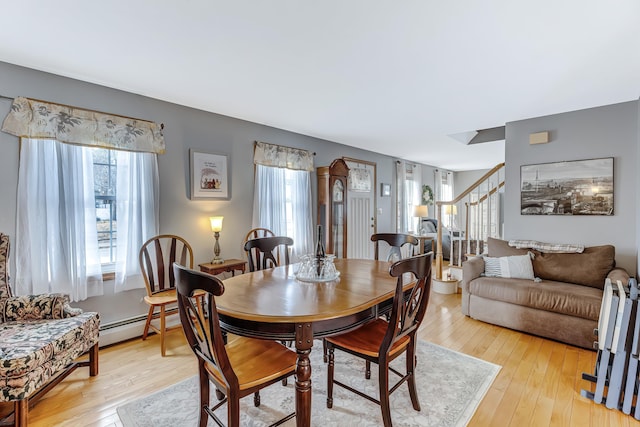 dining area featuring stairs, plenty of natural light, light wood-type flooring, and baseboard heating