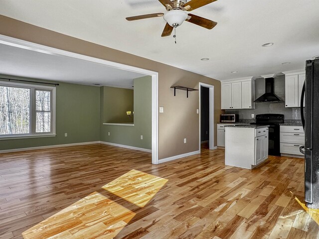 kitchen featuring black appliances, open floor plan, wall chimney exhaust hood, white cabinets, and light wood finished floors