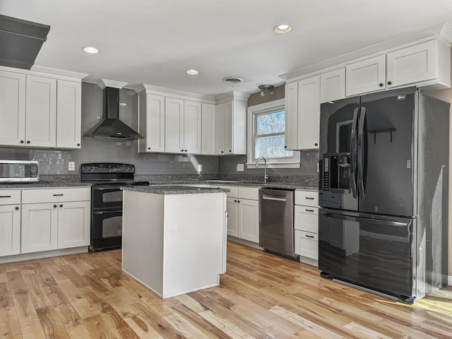 kitchen with light wood-type flooring, black appliances, white cabinets, wall chimney exhaust hood, and tasteful backsplash