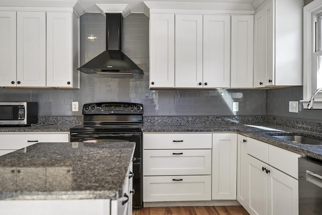 kitchen featuring light wood finished floors, appliances with stainless steel finishes, white cabinets, wall chimney exhaust hood, and a sink