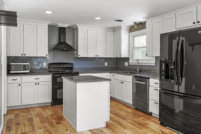 kitchen featuring visible vents, a sink, black appliances, wall chimney range hood, and light wood-type flooring