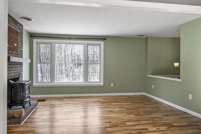 unfurnished living room featuring a wood stove, wood finished floors, visible vents, and baseboards