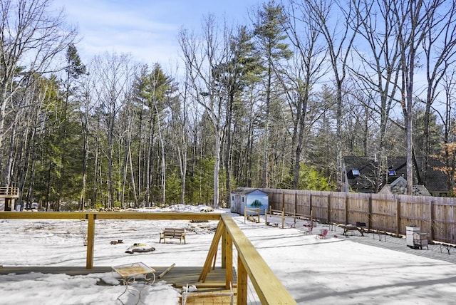 deck featuring a storage unit, a fenced backyard, a view of trees, and an outdoor structure