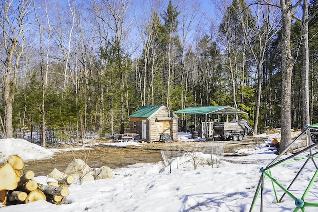 yard layered in snow with an outbuilding, a garage, a forest view, and a storage unit