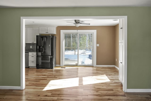 kitchen featuring baseboards, black fridge with ice dispenser, light wood-style floors, dishwasher, and backsplash