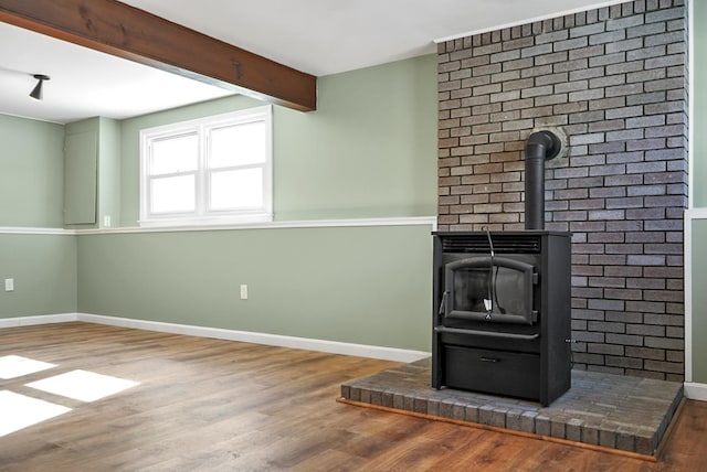 interior space featuring beamed ceiling, a wood stove, baseboards, and wood finished floors