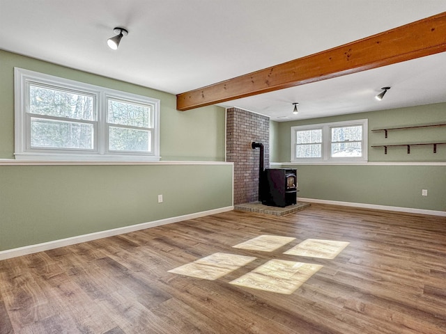 interior space featuring beam ceiling, a wood stove, baseboards, and wood finished floors