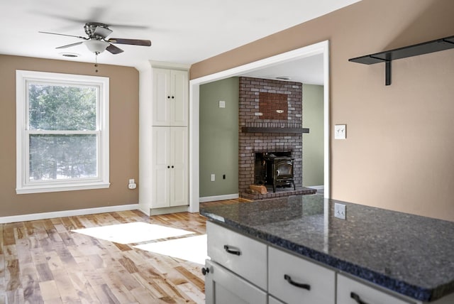 kitchen featuring baseboards, light wood-style flooring, dark stone countertops, white cabinets, and a ceiling fan