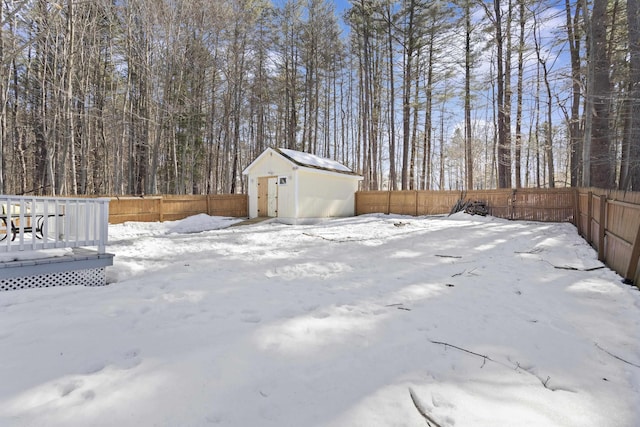 yard layered in snow with an outbuilding, a fenced backyard, a shed, and a wooden deck