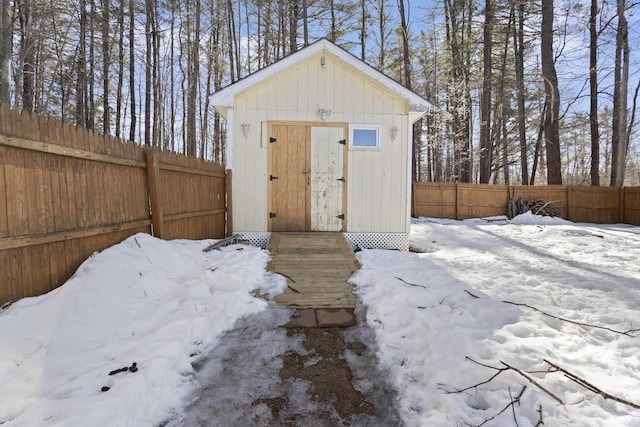 snow covered structure with an outbuilding, a fenced backyard, and a storage shed