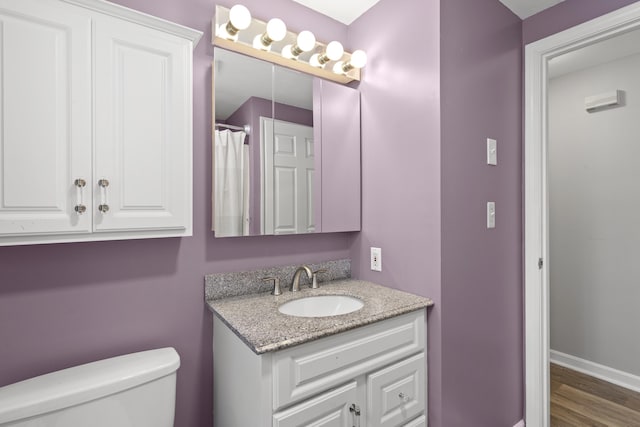 bathroom featuring toilet, vanity, baseboards, and wood finished floors