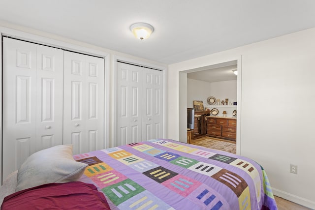 bedroom with baseboards, multiple closets, and light wood finished floors