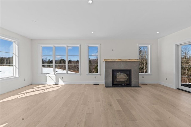 unfurnished living room with plenty of natural light, light wood-style flooring, and a fireplace with flush hearth