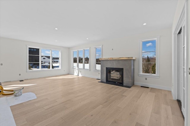 unfurnished living room with recessed lighting, baseboards, a fireplace with flush hearth, and light wood-style floors