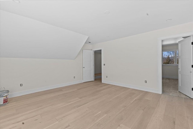 bonus room with light wood-style flooring, lofted ceiling, and baseboards