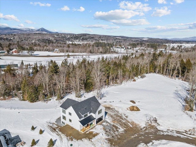 snowy aerial view featuring a wooded view and a mountain view