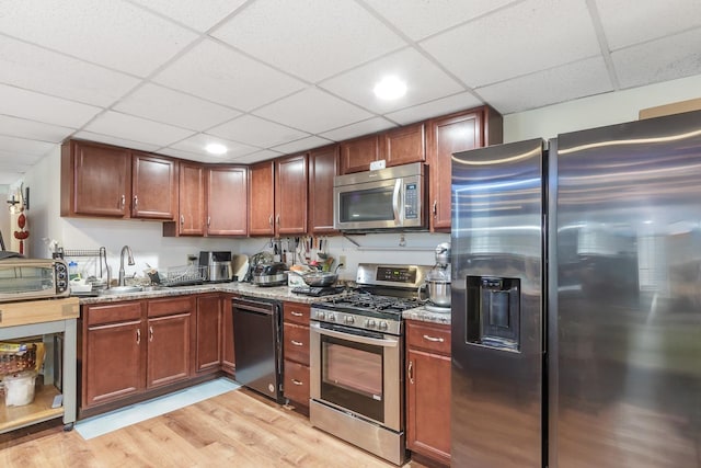 kitchen with light stone countertops, light wood-style flooring, appliances with stainless steel finishes, a paneled ceiling, and a sink