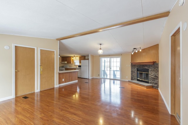 unfurnished living room featuring visible vents, baseboards, light wood finished floors, vaulted ceiling with beams, and a stone fireplace