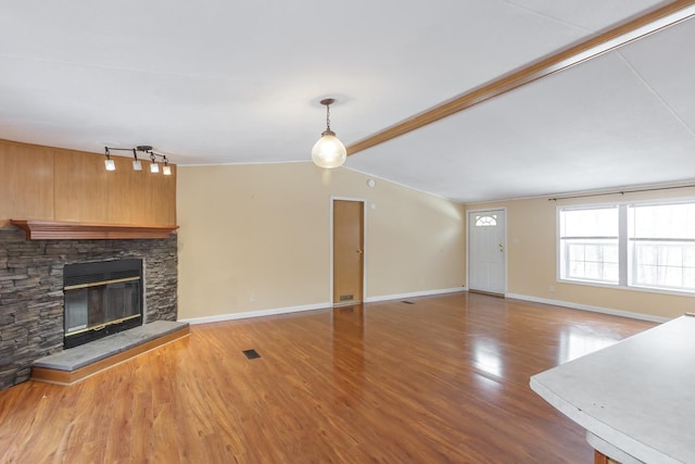 unfurnished living room with wood finished floors, baseboards, visible vents, lofted ceiling with beams, and a stone fireplace