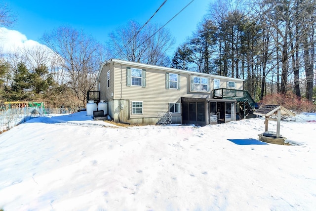 snow covered rear of property with stairs and a sunroom