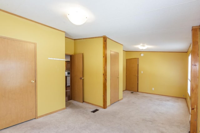 empty room with crown molding, light colored carpet, baseboards, and visible vents