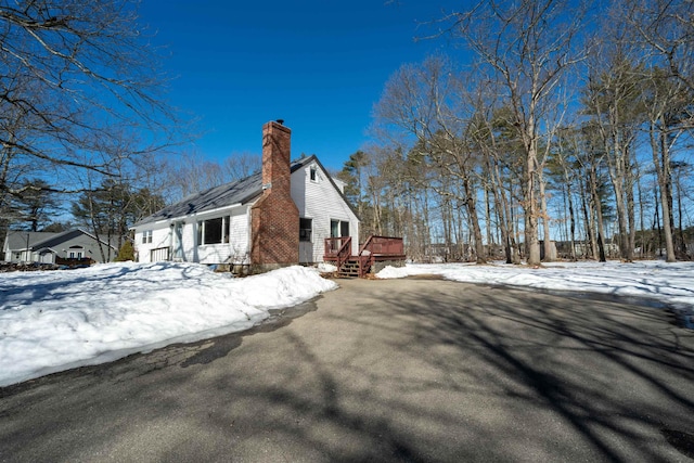 view of snowy exterior featuring a deck and a chimney