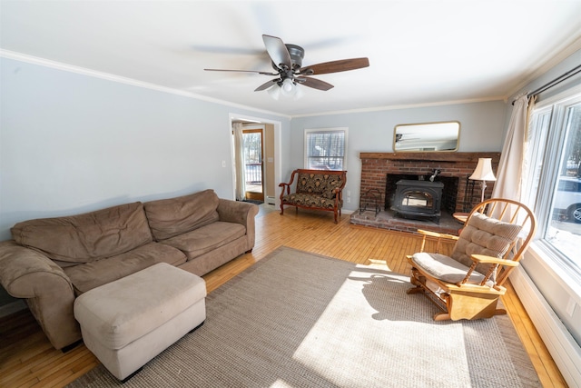 living area featuring ceiling fan, wood finished floors, a wood stove, and ornamental molding