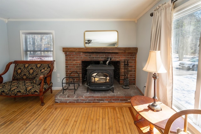 living area with baseboards, ornamental molding, a wood stove, and hardwood / wood-style flooring