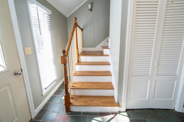 stairway with stone tile floors, crown molding, and baseboards