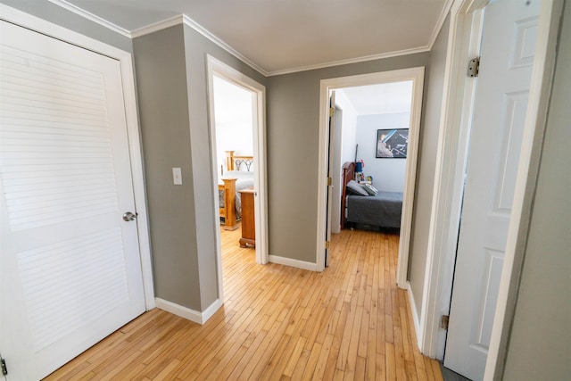 hall with crown molding, light wood-style flooring, and baseboards