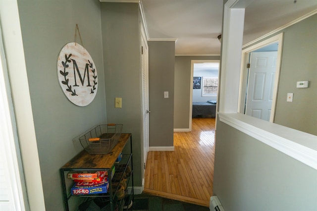 hallway with a baseboard radiator, baseboards, crown molding, and light wood finished floors