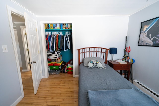 bedroom with a baseboard heating unit, a closet, wood-type flooring, crown molding, and baseboards