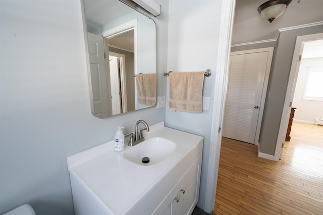 bathroom with baseboards, wood finished floors, vanity, and crown molding