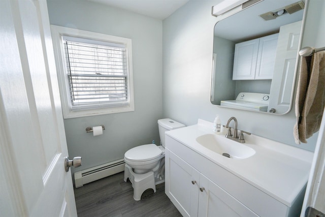 bathroom with toilet, baseboard heating, washer / dryer, wood finished floors, and vanity