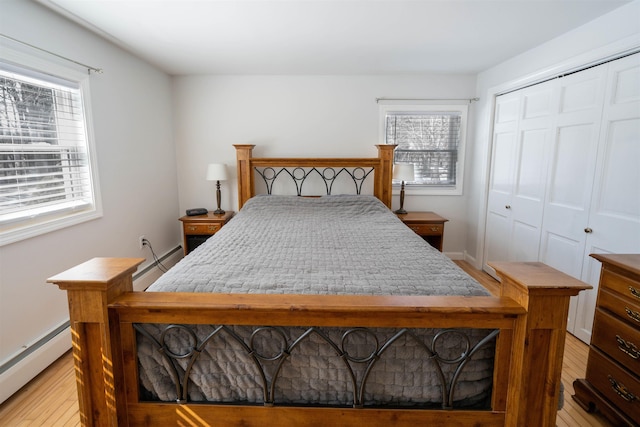 bedroom with a baseboard radiator, baseboards, a closet, and light wood finished floors