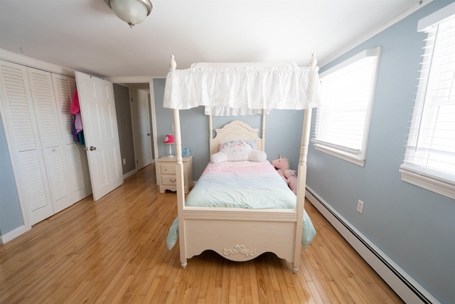 bedroom featuring a closet, light wood-type flooring, a baseboard heating unit, and baseboards