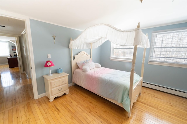 bedroom with baseboard heating, crown molding, and light wood-style floors