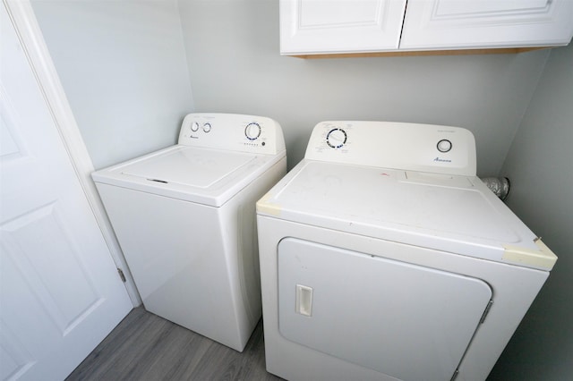 clothes washing area featuring wood finished floors, cabinet space, and washer and clothes dryer