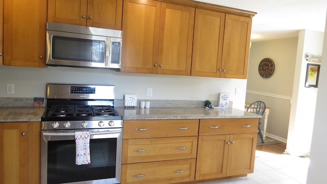 kitchen featuring brown cabinets, appliances with stainless steel finishes, baseboards, and light stone countertops