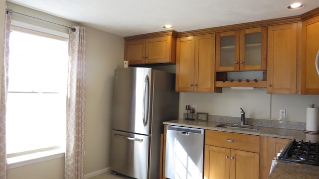 kitchen featuring a sink, glass insert cabinets, appliances with stainless steel finishes, and brown cabinetry