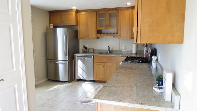 kitchen featuring glass insert cabinets, light tile patterned floors, appliances with stainless steel finishes, brown cabinetry, and a sink